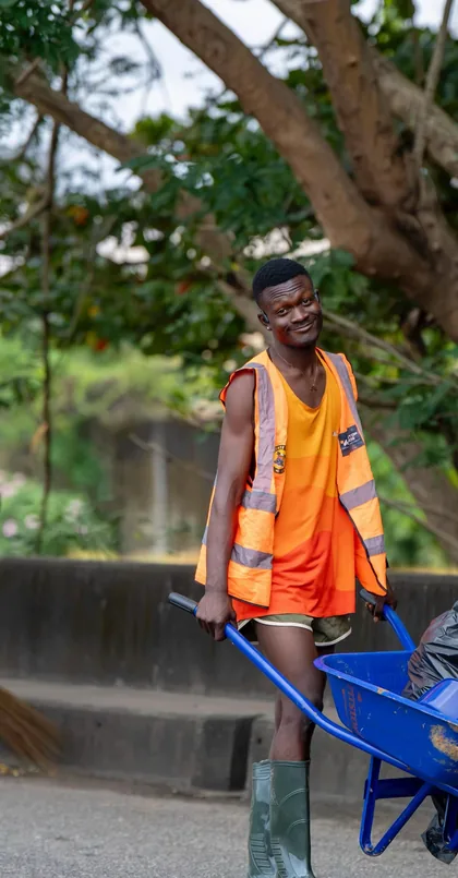A worker pushing a wheelbarrow of collected waste through a Lagos street.